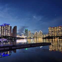 Illuminated buildings by river against sky at night