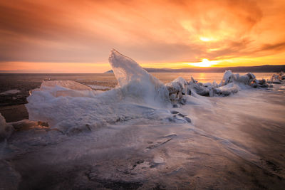 Scenic view of frozen sea against dramatic sky during sunset