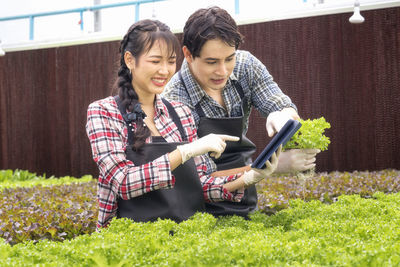 Young woman looking at camera while using phone by plants