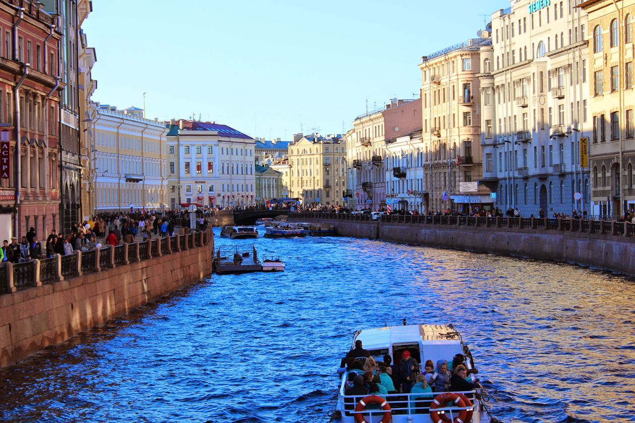 architecture, building exterior, built structure, water, canal, large group of people, waterfront, men, city, nautical vessel, residential building, clear sky, person, building, boat, lifestyles, transportation, city life, residential structure