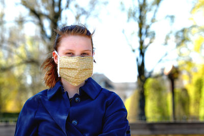 Portrait of woman covering mask sitting in park
