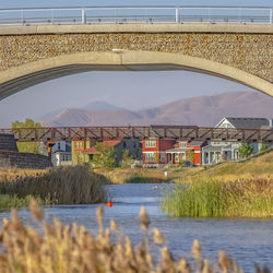 Arch bridge over river by houses against sky