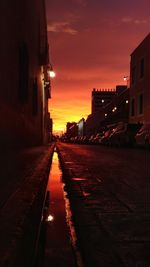 Street amidst buildings against sky at sunset