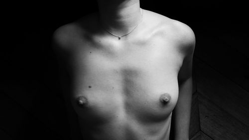 Midsection of shirtless man standing against black background