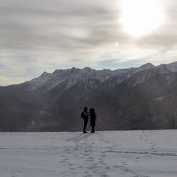 Man and woman standing on snow covered land against mountains and sky