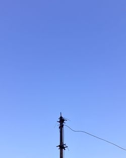 Low angle view of electricity pylon against clear blue sky