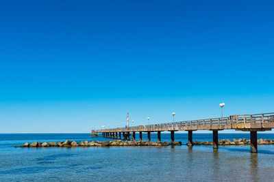 Pier over sea against clear blue sky