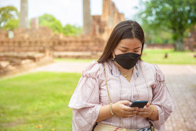 Smiling chubby asian woman using a cell phone while traveling in a buddhist temple in asia.