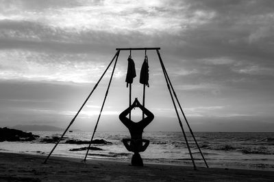 Man doing yoga at beach against sky during sunset