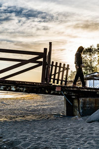 Man standing on pier over sea against sky during sunset