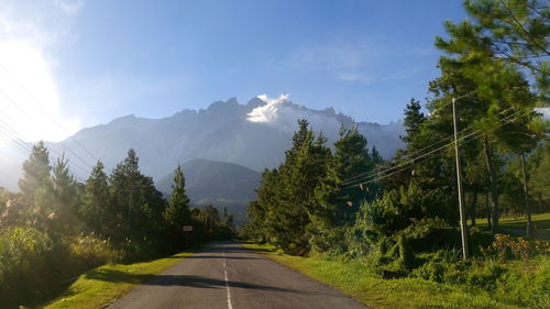 Sunlight falling on empty road amidst trees against mountains