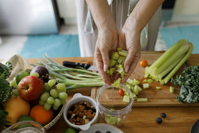 Hands of woman putting chopped celery in juicer at home