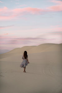 Rear view of woman walking on sand dune