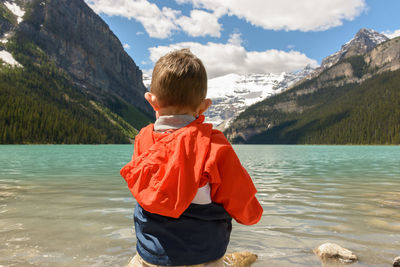 Rear view of boy standing on mountain by lake against sky