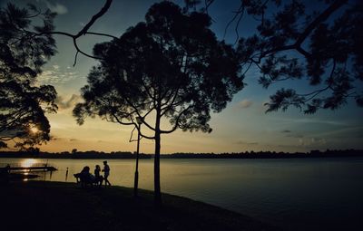 Silhouette people by lake against sky during sunset