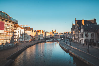 Canal amidst buildings against clear blue sky