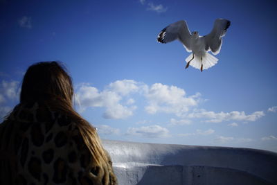 Low angle view of woman with seagulls flying against sky