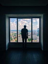 Rear view of man standing by window in room