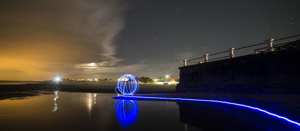 Light trails on bridge against sky at night