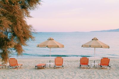 Orange colored chairs and grass parasols  on beach by sea against sky and no people around
