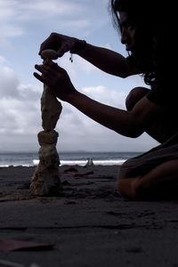 Man stacking pebbles at beach against sky