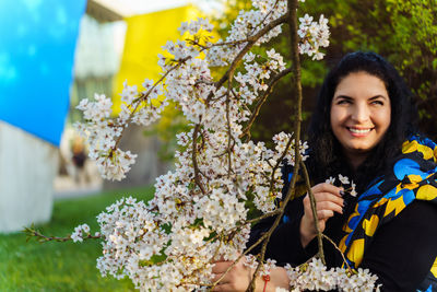 Ukrainian woman getting pleasure and smiling while spending time among flowering trees in city park