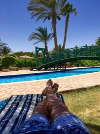 Low section of man relaxing by swimming pool against clear blue sky