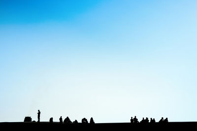 Silhouette people at beach against clear blue sky
