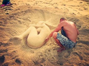 High angle view of shirtless man relaxing on sand at beach