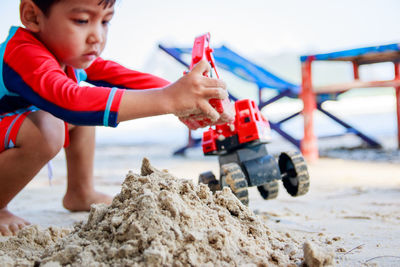 Side view of boy playing with toy at sandy beach