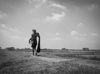 Rear view of people walking on field against sky