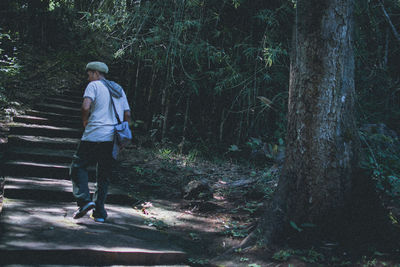 Rear view of man walking on staircase in forest