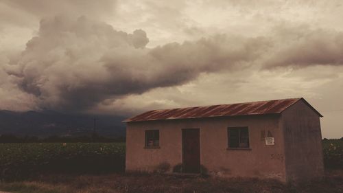 House on field against storm clouds
