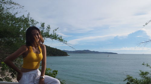 Woman sitting by tree against sky