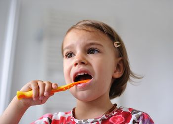 Close-up of girl brushing teeth against wall