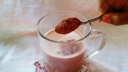 Close-up of hand adding chocolate powder in milk