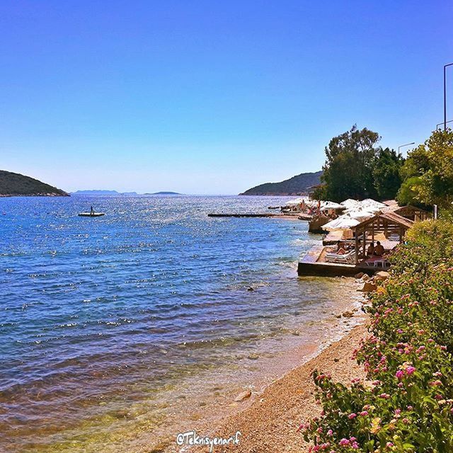 clear sky, copy space, water, blue, sea, building exterior, built structure, beach, architecture, scenics, nature, beauty in nature, horizon over water, tranquil scene, tranquility, shore, tree, sunlight, day, coastline