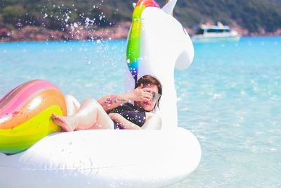 Full length of woman relaxing on inflatable unicorn at sea