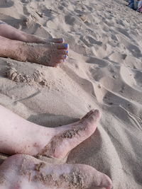 Low section of person relaxing on sand at beach