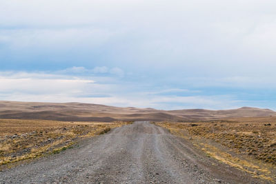 Dirt road amidst land against sky