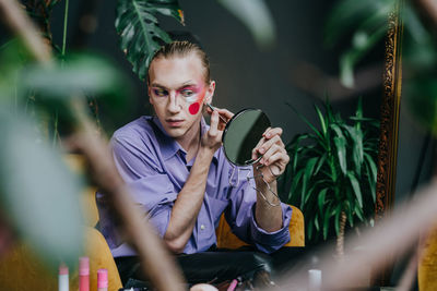 Man applying make-up looking in hand mirror