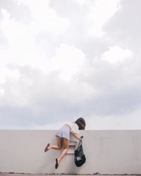 Woman climbing on wall against sky