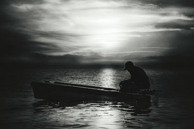 Silhouette man sitting on sea against sky