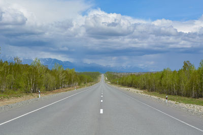 Empty road along plants and trees against sky