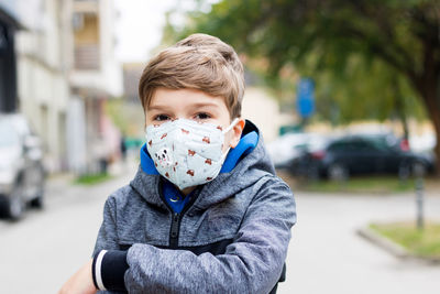 Portrait of boy wearing face mask outdoors during coronavirus pandemic and looking at camera.