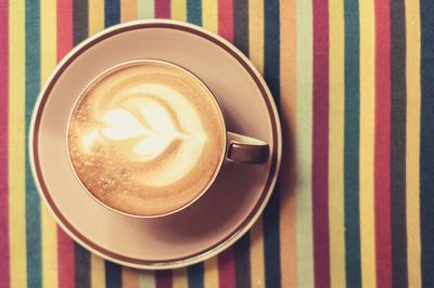 High angle view of coffee cup in plate on colorful tablecloth