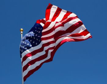 Low angle view of flag against clear blue sky