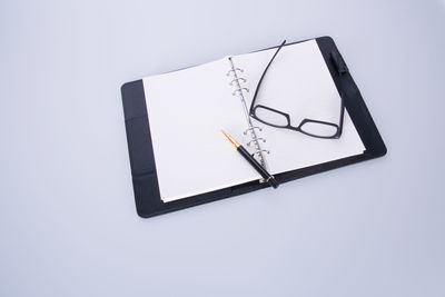 High angle view of book with eyeglasses and pen on white background