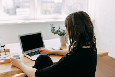 Woman using phone while sitting on table at home