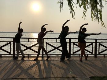 Silhouette female friends dancing on promenade against clear sky during sunset